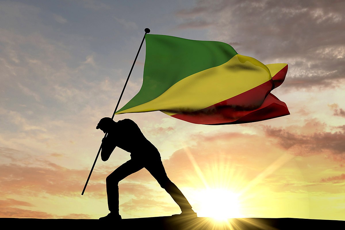 A man walks with the flag of the Republic of the Congo at sunset A man walks with the flag of the Republic of the Congo at sunset