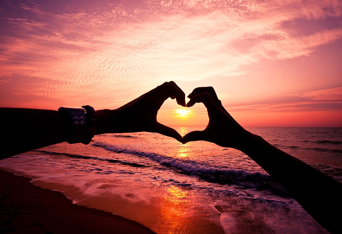 Image of human hands in the shape of a heart at sunset