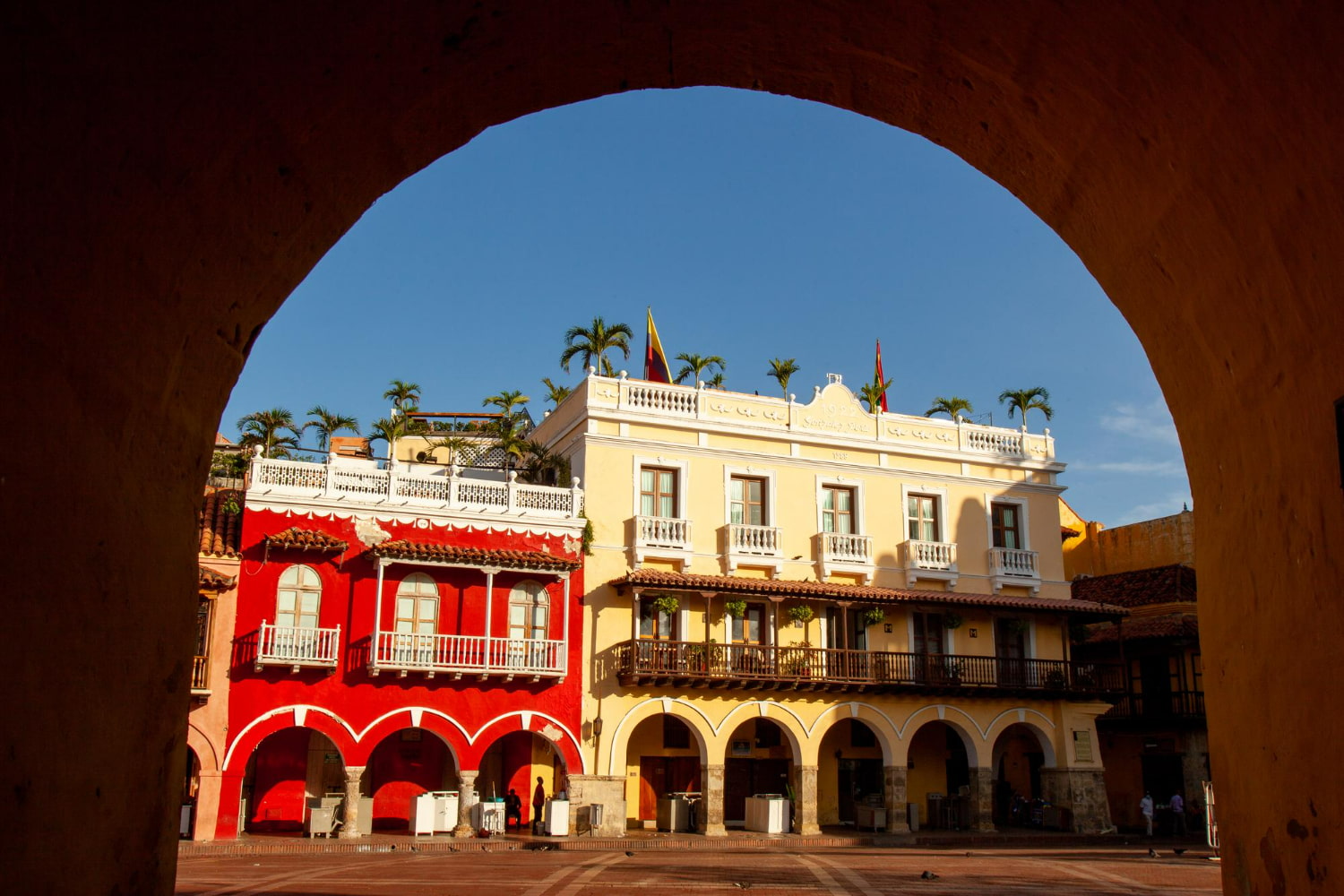 This stunning photograph captures a picturesque colonial plaza in Cartagena, Colombia, beautifully framed through an ancient archway.