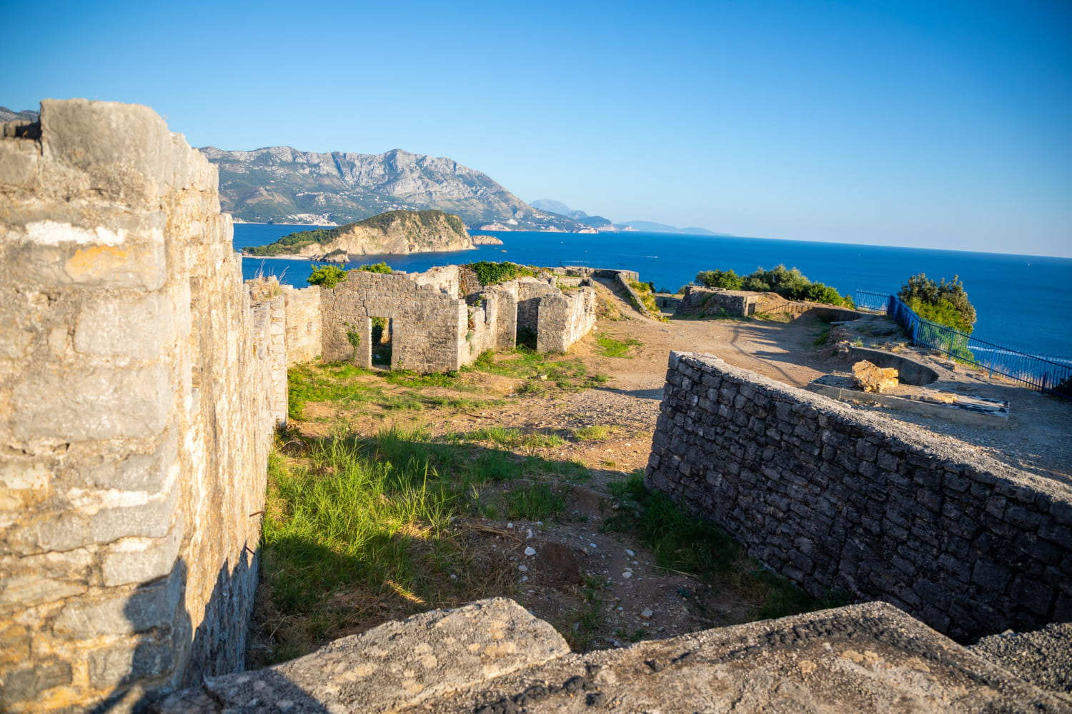 Nature has softly reclaimed these structures, with green grass and wildflowers sprouting between the ancient stones.