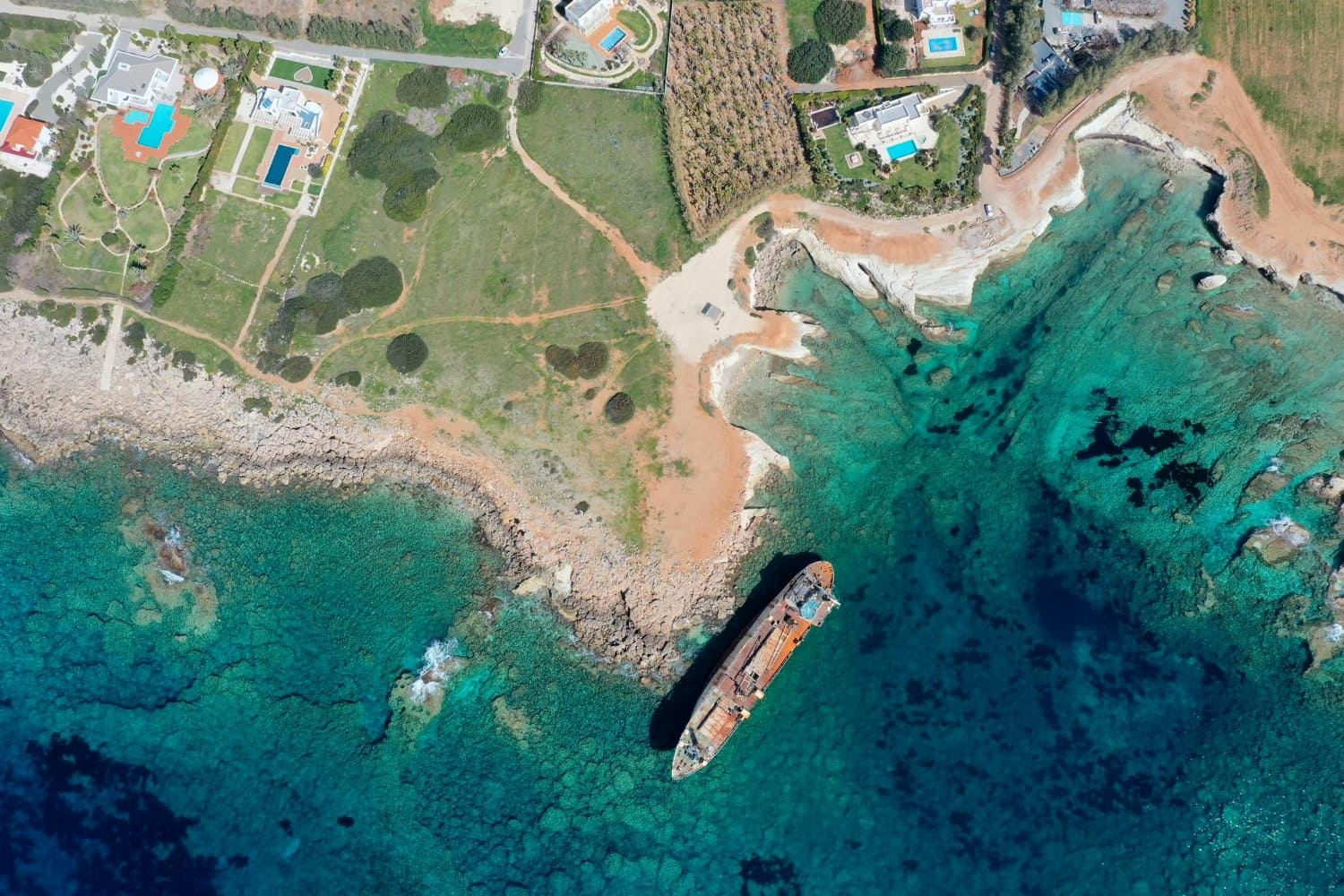 The ship's deteriorated hull, stained with rust and oxidation, creates a striking contrast against the impossibly clear waters that surround it.
