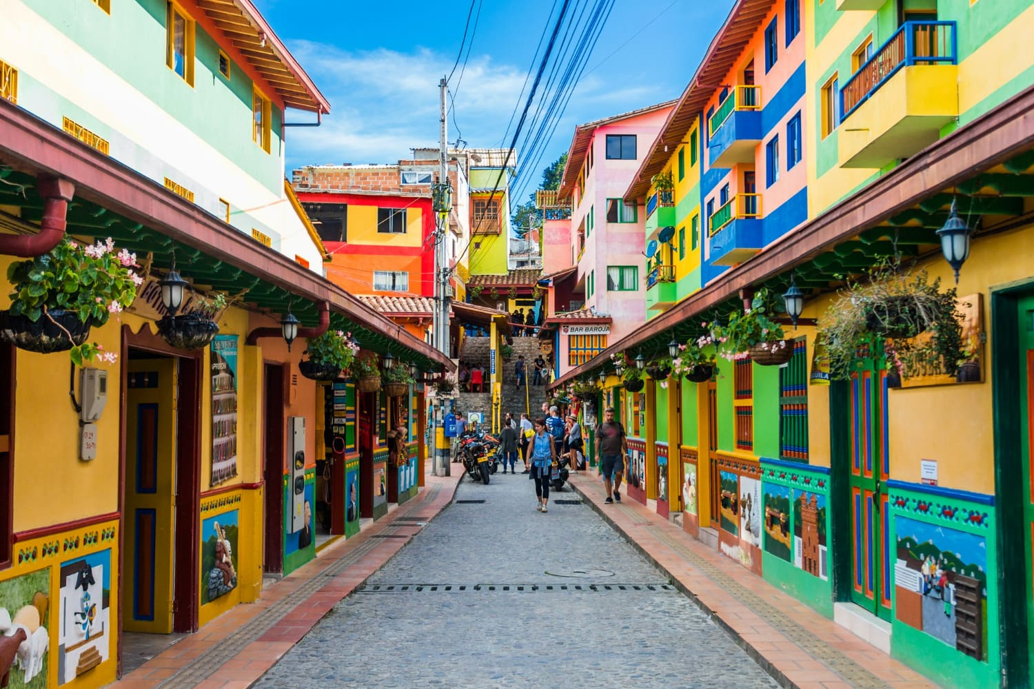 The image showcases a lively pedestrian street lined with brilliantly painted colonial buildings that form a rainbow of colors.