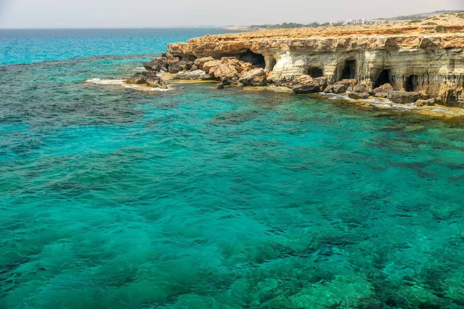 This breathtaking coastal photograph showcases a Mediterranean paradise where dramatic natural sea caves meet impossibly clear turquoise waters.