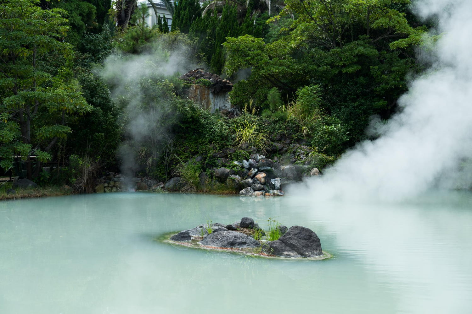 A mesmerizing geothermal landscape showcases ethereal wisps of steam rising from vibrant turquoise mineral-rich hot springs surrounded by lush, verdant vegetation.