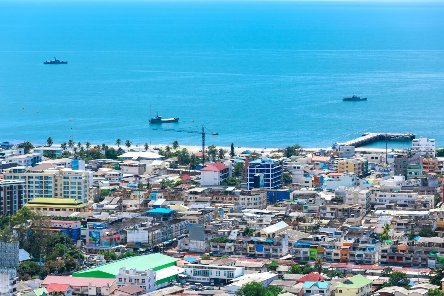 This stunning aerial perspective captures a vibrant tropical coastal town nestled between emerald vegetation and crystalline turquoise waters.