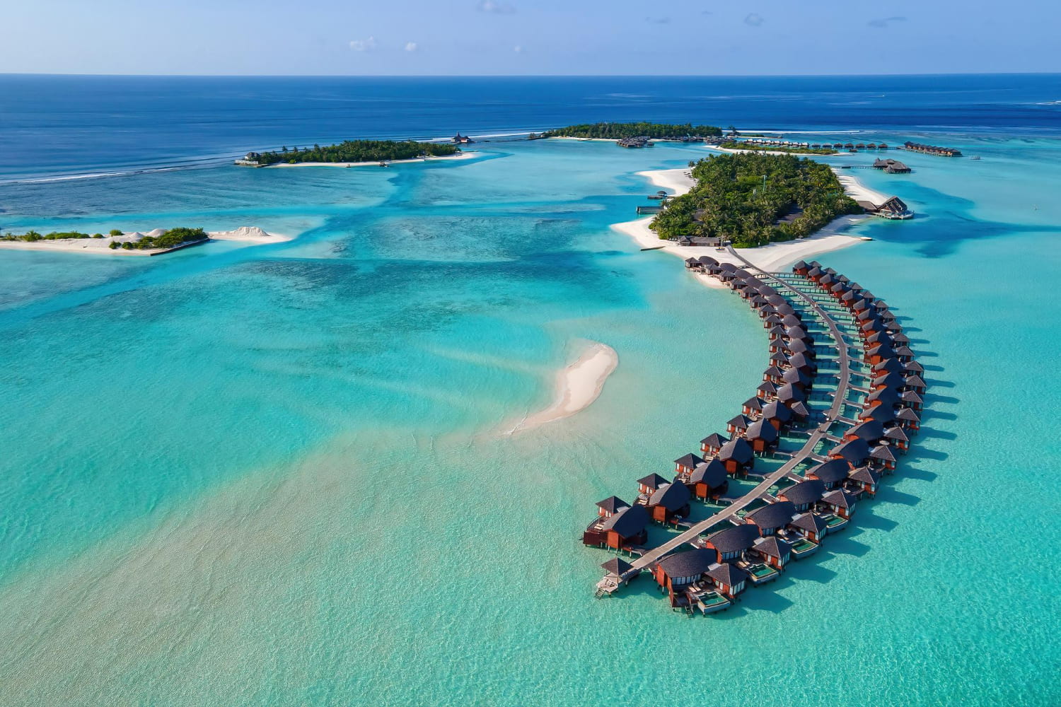 This stunning aerial photograph showcases an exclusive overwater bungalow resort nestled in a tropical island paradise.